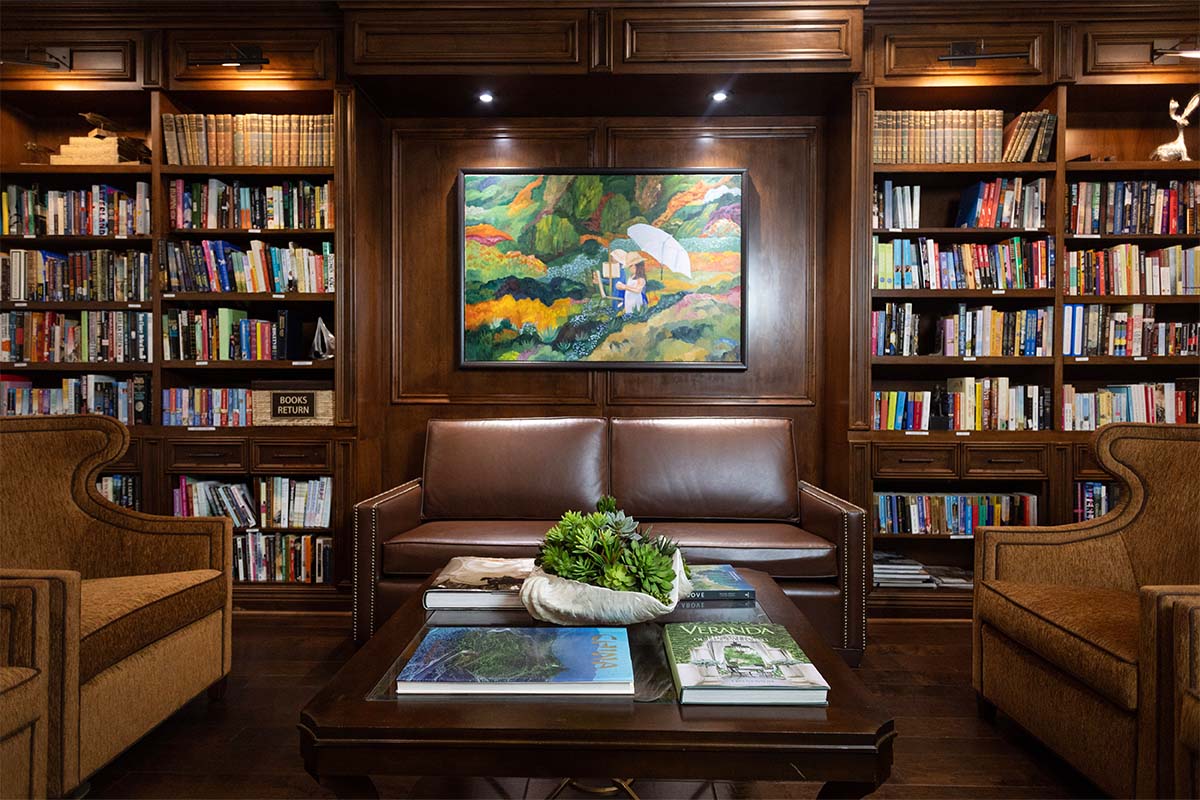 Crestavilla's reading area with dark wood bookshelves and floors, artwork on the walls, and plenty of comfortable seating.