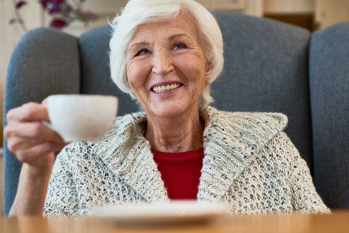 Smiling woman in a handsome knit sweater holding up a cup of tea.