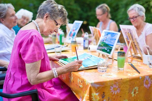 Group of older ladies seated around a table painting with watercolors.