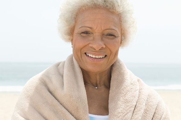 Smiling older African American woman wrapped in a shawl at the beach.