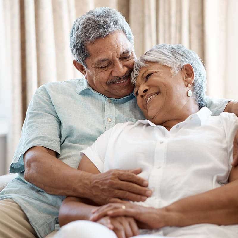 Older Hispanic couple cuddling on a couch.