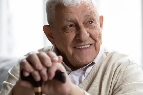 Older man smiling and resting his hands atop a cane.