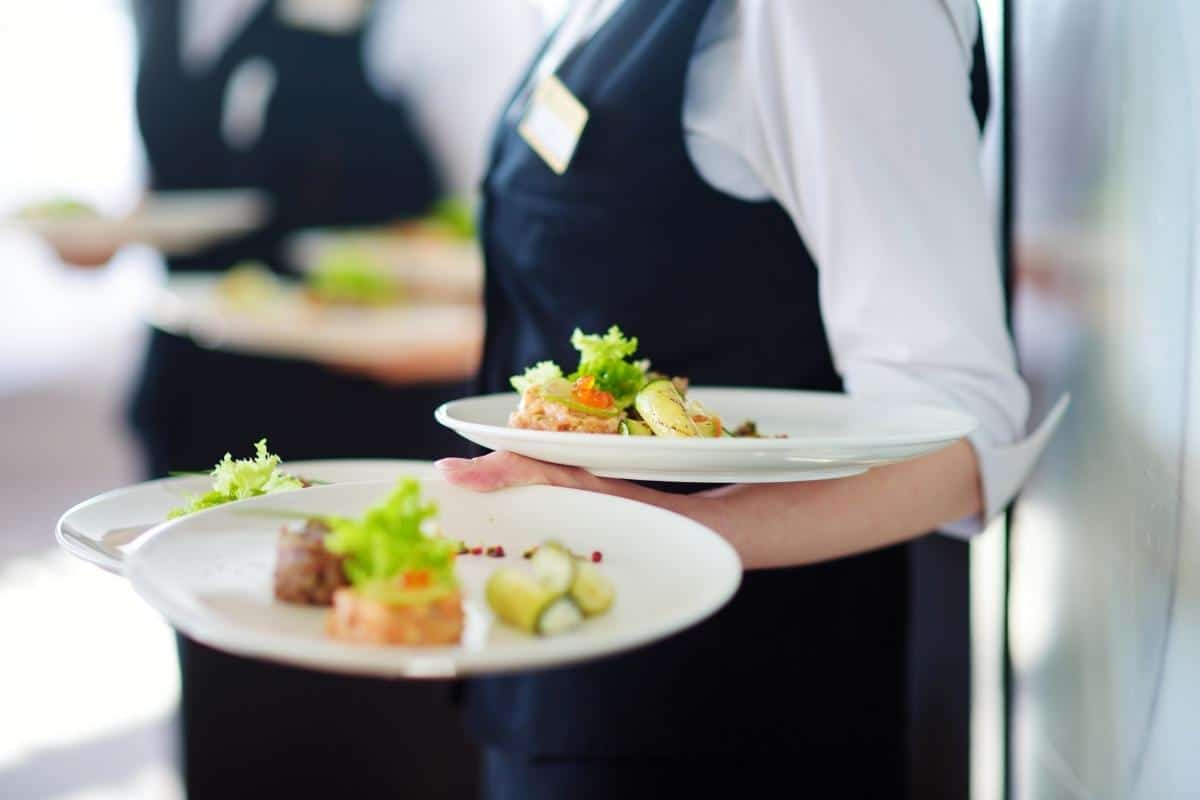 Waiters in black and white attire carrying plates of gourmet food.