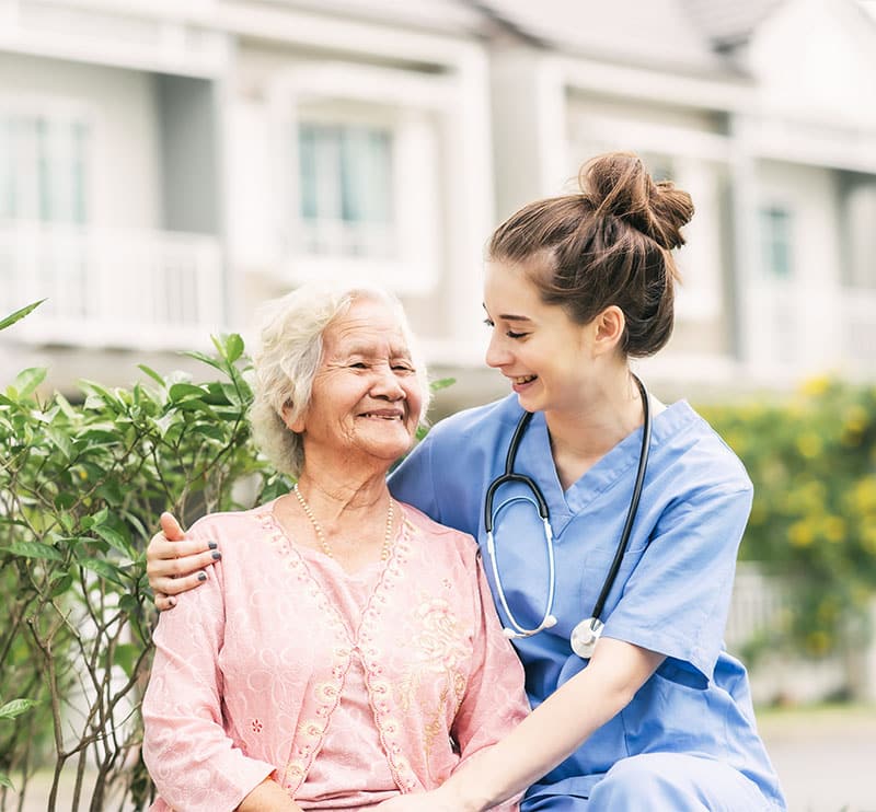 A nurse gently hugs an older Asian woman.