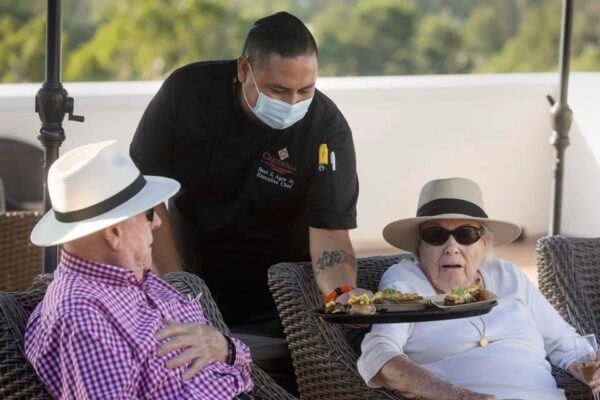 A dining staff member offers two Crestavilla residents hors d'oeuvres at an event on the rooftop.