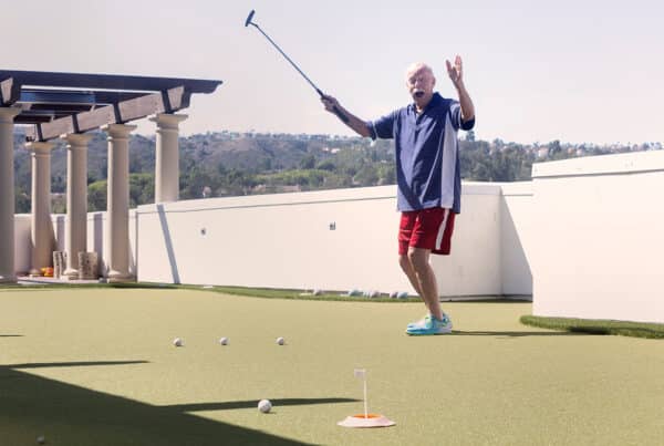 Man on putting green raising his hand and golf club.
