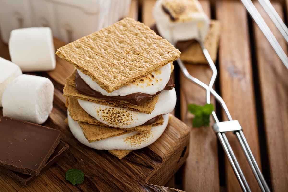 Stack of s'mores, marshmallows and chocolate bars on a wooden table.